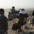 Young children stand and older men sit along a dirt road with an Israeli tank approaching