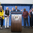 Man speaks from podium with several people looking on