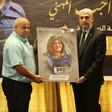 Two men hold framed picture of Shireen Abu Akleh while standing on stage