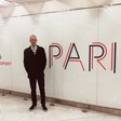 A man stands next to a sign reading Paris Airport and Paris