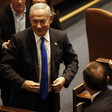 Benjamin Netanyahu smiles while walking and surrounded by other people in suits