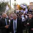 Man wearing suit surrounded by many other people, some of whom wave blue and white flags.