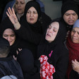 A group of women dressed in headscarves mourning, with one woman stretching her arms out