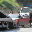 Two men, one wearing police uniform, load a car onto a tow truck with police vehicle behind them