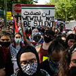 A group of protesters hold signs and Palestine flags. One banner reads We Will Not Be Silent in English and Arabic.