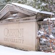 Snow and bushes surround a stone sign with the name of the university
