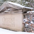 Snow and bushes surround a stone sign with the name of the university