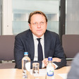 Olivér Várhelyi, a member of the European Commission, sits at a desk with a glass and bottles of water