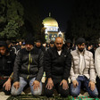 A group of mean kneels in prayer with golden dome behind them