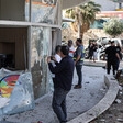 Men stand in front of building with broken and shrapnel-pocked windows