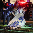 Officers, one wearing a hazmat suit, lift tarp over body lying on ground
