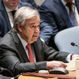 António Guterres holds a piece of paper while sitting at conference table in front of microphone