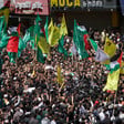 A crowd of hundreds fly faction flags as two shrouded bodies are carried on stretchers