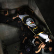 People carry a corpse wrapped in a flag down a staircase 
