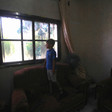 A small boy in dark room looks out of window with broken glass
