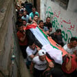 Men in a narrow alleyway carry a stretcher draped in a Palestinian flag