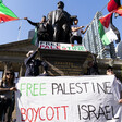 ctivists hold a large free palestine banner and flags in front of a statue and a neo-classical building