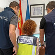 Two people, one wearing a vest reading Interpol, the other wearing a vest reading Europol stand on either side of a seated person wearing a vest reading Cuerpo Nacional de Policia 