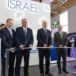 Israel's Defense Minister Yoav Gallant and a number of other men hold a scissors to a ribbon with a sign reading Israel in large letters behind them