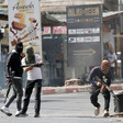 Three men wearing street clothes with their faces covered carry rifles in street