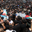 A crowd of dozens carry two bodies on stretchers wrapped in Palestine flags and kuffiyehs