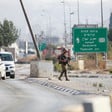 Soldier carrying rifle walks on median with Palestinian-plated cars in one lane and an empty lane on the other side