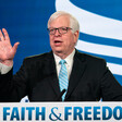 Dennis Prager raises his hand at podium before a faith and freedom sign