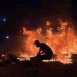 The silhouette of a man wearing a cap against the backdrop of fire and burning tires 