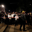 Men and boys in Orthodox Jewish dress stand behind police tape at night
