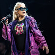 Christina Aguilera, in a purple jacket and wearing sunglasses, holds a microphone