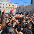 Crowd of men carry shrouded body on stretcher