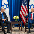 Joe Biden raises his right hand while sitting in chair opposite from a seated Netanyahu with US and Israeli flags behind them
