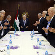 Men, some in uniform and others in suits, stand around a meeting table with Abbas at its head