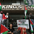 People holding signs and flags appear to be listening to a speaker who is not visible in the picture