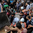 A crowd of men including rescue workers carry a man on a stretcher next to the scoop of an excavator machine