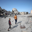 Two people are seen walking amid ruins of large apartment buildings