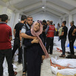 A man wraps his arm around a crying woman as they stand in a tent surrounded by shrouded bodies lying on the ground