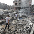 Young people walk on rubble in front of bombed-out residential building