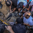 Men, most with bare hands, hold the body of a man partially buried in sandy rubble