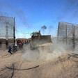 Excavator scoop moves through empty space in fence covered with barbed wire