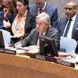 Antonio Guterres holds a piece of paper while sitting at a table with a microphone in front of him