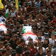 A massive crowd of people carries two bodies wrapped in flags 
