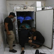 Men inspect a fridge with bodies in it at a morgue 