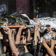 A view of hands carrying bodies wrapped in flags on stretchers while others hold rifles 