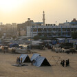 Landscape view of people standing next to several tents in front of school and sky with a yellow glow