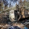 Burned out, overturned bus lies amid debris and trees