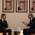 Two men in suits sit across from each other in reading chairs conversing 