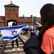 A person carries an Israeli flag in front of a brick building that is part of the former Auschwitz death camp