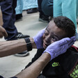 A doctor, wearing gloves, cradles the face of a small wounded child on the floor of a hospital 