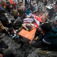 A child partly covered by a blanket is carried on a stretcher by several people amid a large crowd
